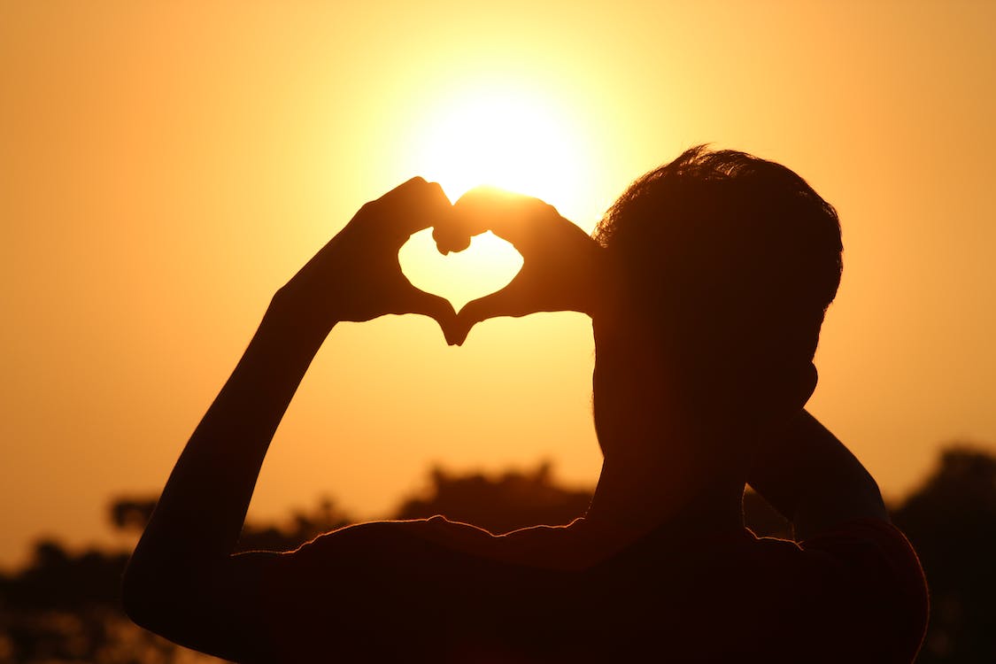 image of man in sunset making heart shape with hands